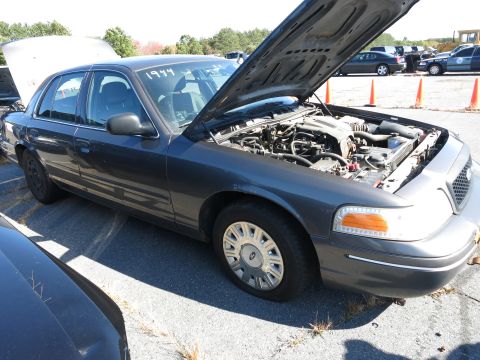 2001 Ford Crown Victoria - A dark gray sedan is parked with its hood open, revealing the engine compartment. The number '1999' is written on the windshield.