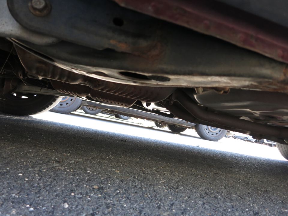 Underside view of a car showing the exhaust system, frame, and wheels of multiple vehicles parked nearby