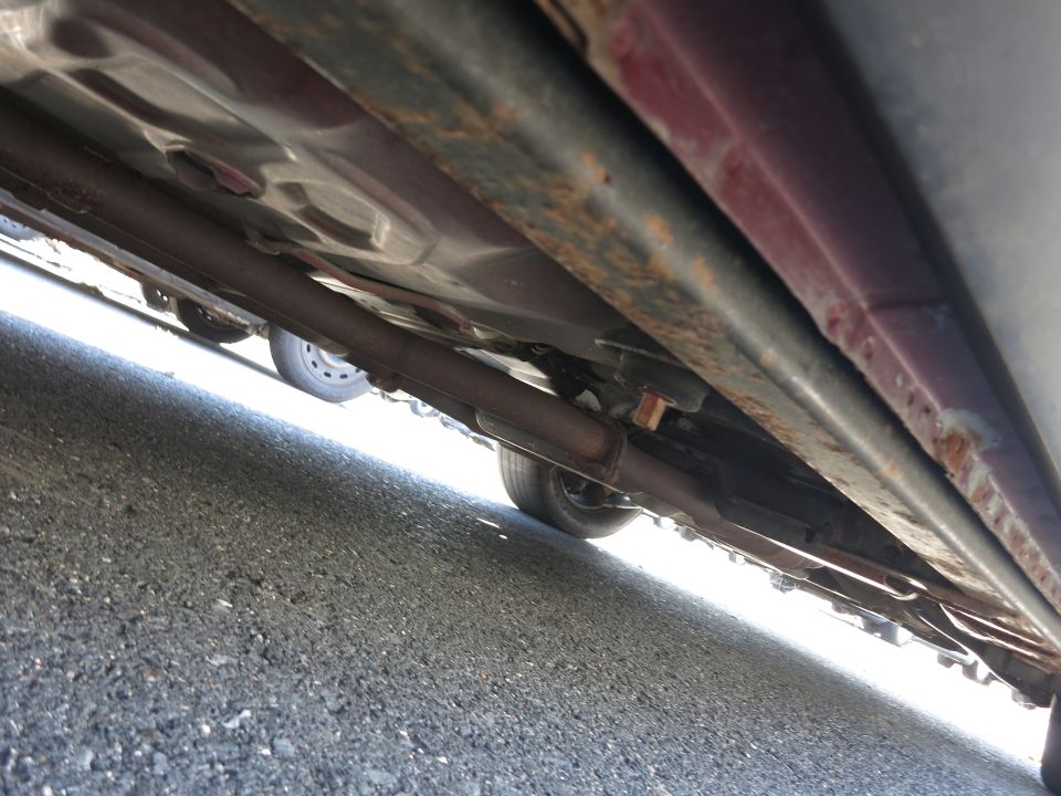 Underside view of a car's frame and exhaust system, showing some rust