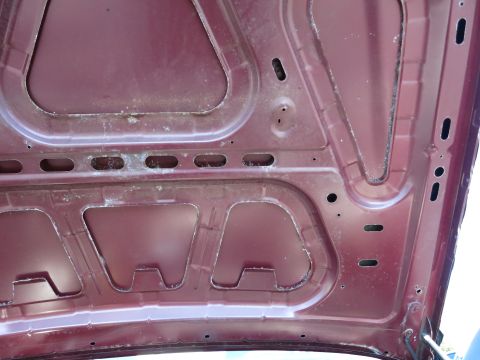 2001 Ford Crown Victoria - The underside of a maroon car hood shows structural bracing and signs of wear.