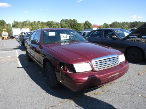 2001 Ford Crown Victoria - A maroon 2001 Ford Crown Victoria is parked in a lot with other vehicles under a clear sky.