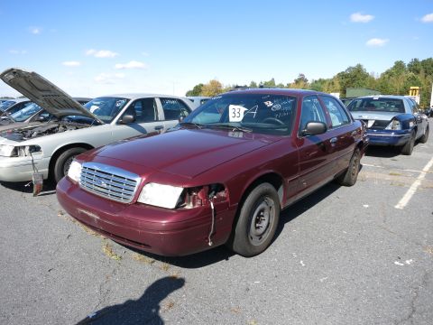 2001 Ford Crown Victoria - Maroon 2001 Ford Crown Victoria in a lot, showing damage to the front end and missing headlights.