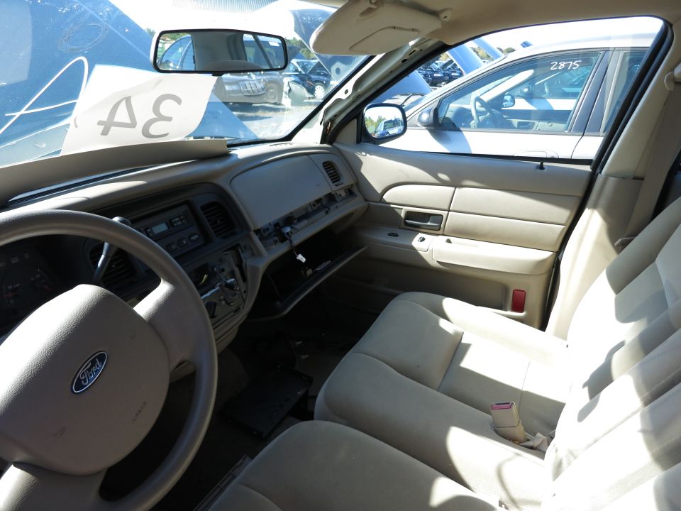 Interior view of a 2001 Ford Crown Victoria, showing dashboard, steering wheel with Ford logo, and front seats. Other vehicles visible through windows