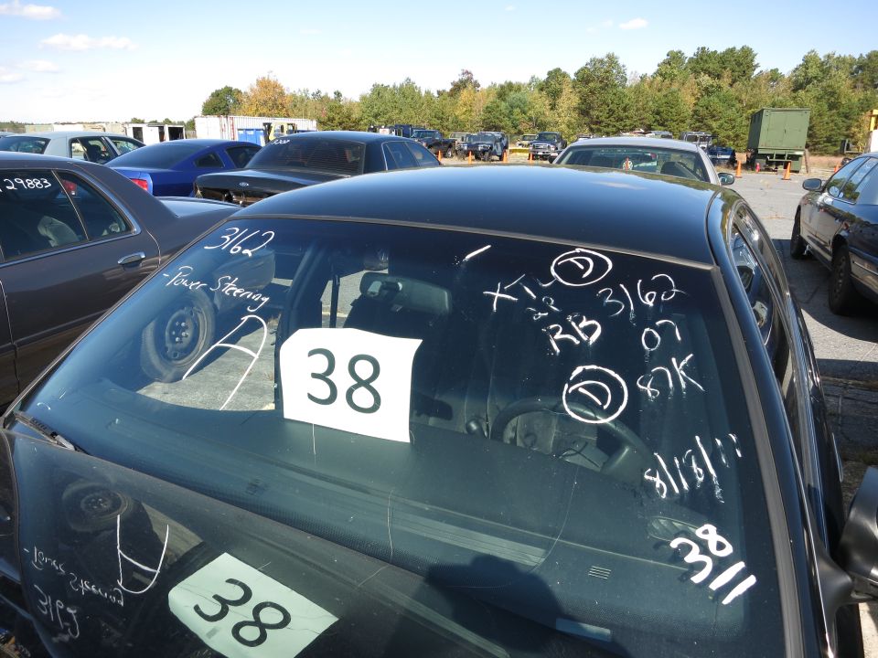 Interior view of a black sedan showing windshield markings including '3162', 'Power Steering', 'XT L 3/62', 'RB 3/62 07 87K', and '8/31/11'. Two white signs with '38' are visible