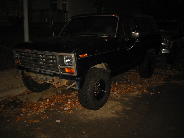 Dark colored Ford Bronco with aftermarket wheels and tires. Another vehicle is parked behind it