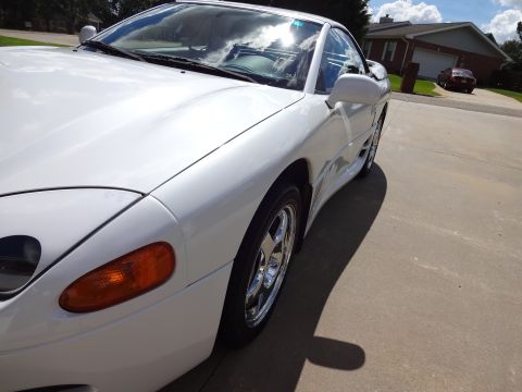 1995 Mitsubishi 3000GT - A white 1995 Mitsubishi 3000GT is parked on a concrete driveway under a partly cloudy sky.