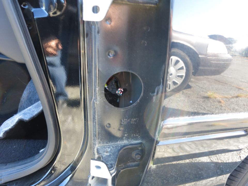 Close-up of a black car's door jamb with a glimpse of another car's wheel and front end in the reflection