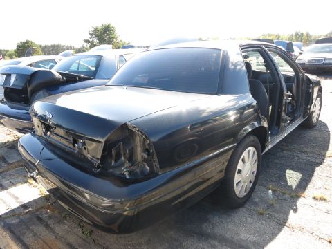 2001 Ford Crown Victoria - Junkyard sedan, likely a 2001 Ford Crown Victoria, with missing taillights and open door.