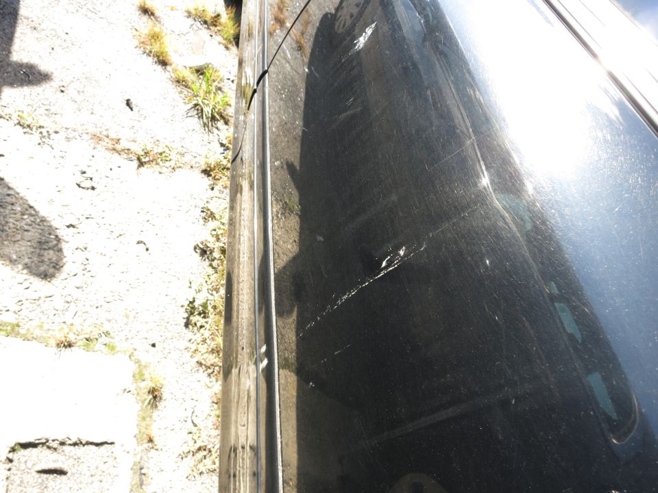 Black car door with scratches and dents, viewed from the side