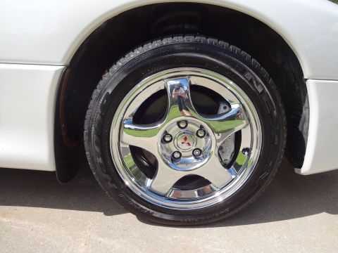 1995 Mitsubishi 3000GT - Close-up of a 1995 Mitsubishi 3000GT's front wheel, a chrome five-spoke rim with the Mitsubishi logo and 'MITSUBISHI' branded brake caliper…