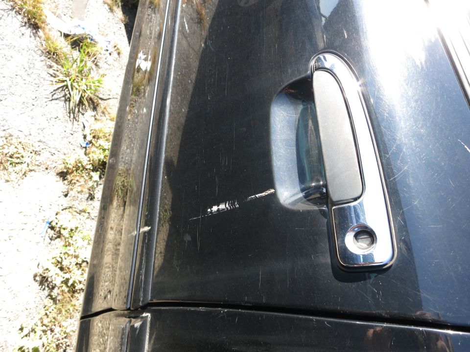 Close-up of a black car's side panel with a chrome door handle and visible scratches