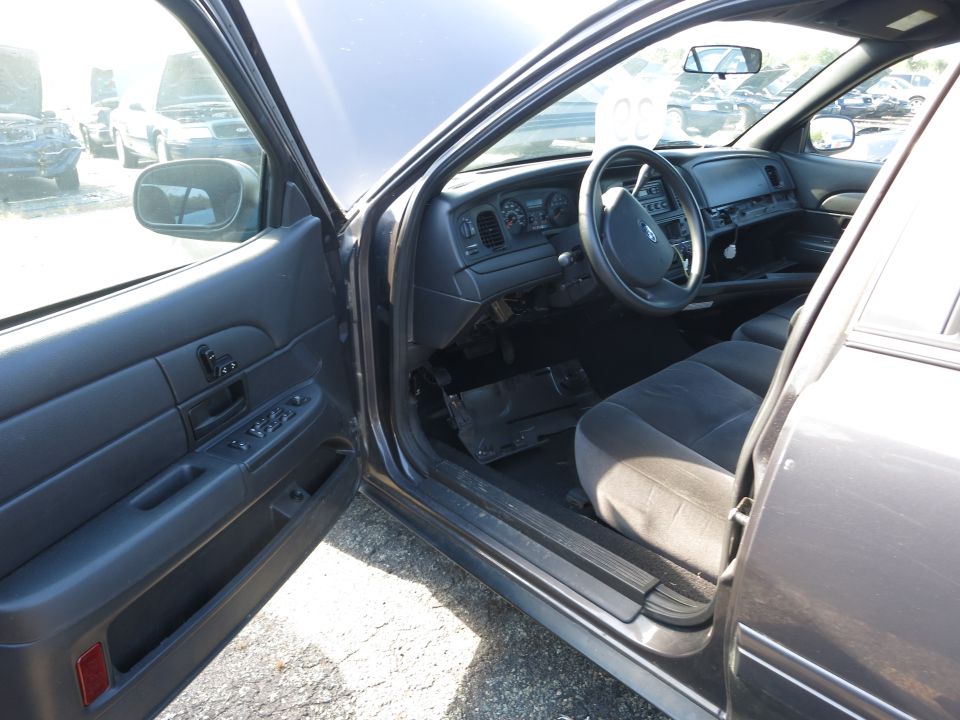 Interior of a dark-colored sedan with the driver's door open. Dashboard, steering wheel, and seats are visible. Other cars are in the background