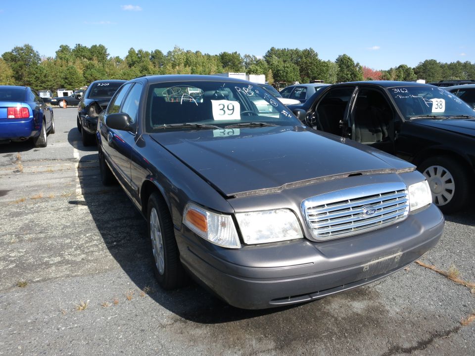 Dark gray 2001 Ford Crown Victoria, front 3/4 view, hood ajar, with a "39" sign on the windshield