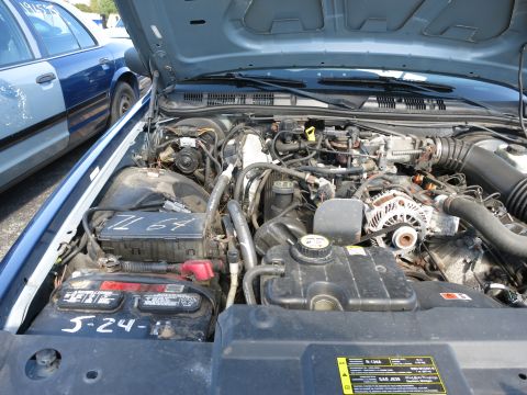 2001 Ford Crown Victoria - The engine bay of a blue vehicle is shown, with a battery visible and labeled with a date. Another blue and white vehicle is partially visi…
