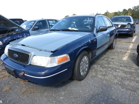2001 Ford Crown Victoria - A blue Ford Crown Victoria, possibly a 2001 model, sits in a lot with its hood up and other vehicles nearby.