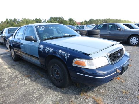 2001 Ford Crown Victoria - A 2001 Ford Crown Victoria, showing significant wear and tear, is parked outdoors with other vehicles visible in the background.