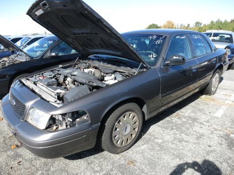 2001 Ford Crown Victoria - A dark gray 2001 Ford Crown Victoria sedan is parked with its hood open, revealing the engine compartment and front wheel.