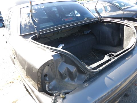 2001 Ford Crown Victoria - The rear of a dark sedan is shown with its trunk open, revealing an empty cargo area and a missing taillight.