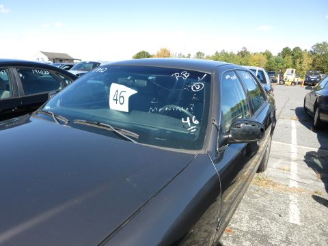 2001 Ford Crown Victoria - A dark sedan is parked in a lot with other vehicles and a building in the background.