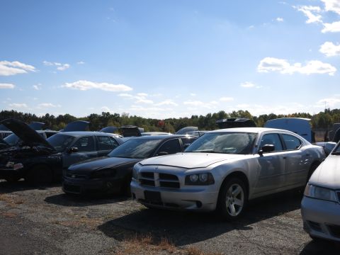 2001 Ford Crown Victoria - A silver Dodge Charger sits in a car lot under a blue sky with scattered clouds.