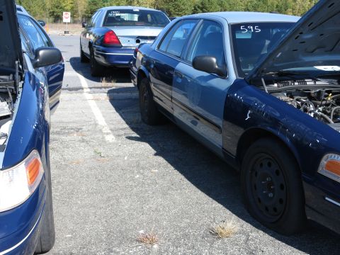 2001 Ford Crown Victoria - Multiple Ford Crown Victoria police cars are parked in a lot, with two showing their open hoods.