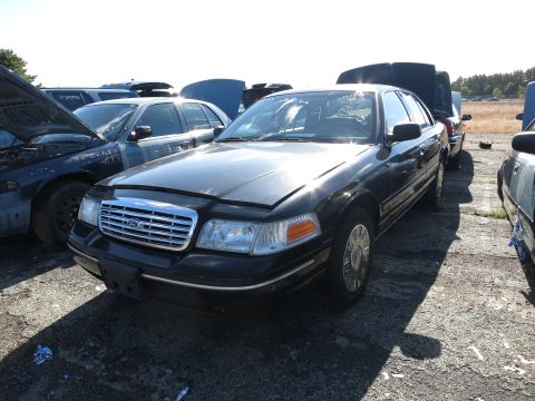 2001 Ford Crown Victoria - Junkyard scene with a black 2001 Ford Crown Victoria in the foreground.