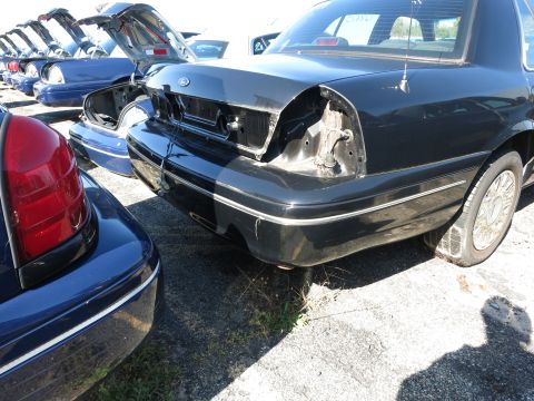 2001 Ford Crown Victoria - Rear view of a black 2001 Ford Crown Victoria with damaged rear end, parked in a vehicle lot.