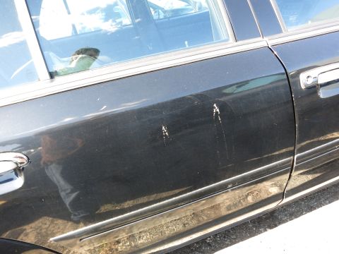 2001 Ford Crown Victoria - Scratches mar the side of a black sedan, with a reflection visible in the window.