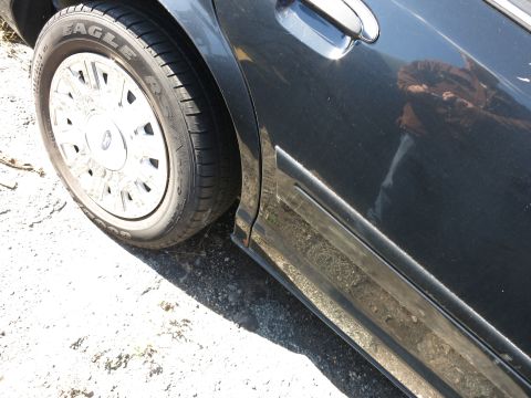 2001 Ford Crown Victoria - Close-up of the side of a dark sedan, highlighting the wheel and door panel.