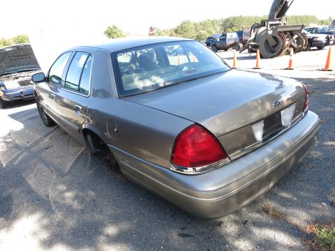 2001 Ford Crown Victoria - A tan 2001 Ford Crown Victoria is parked outside with another vehicle in the background.