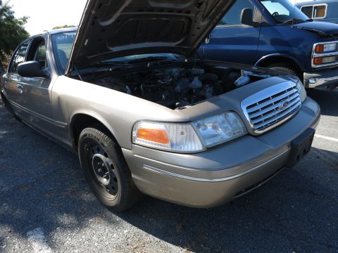 2001 Ford Crown Victoria - A tan 2001 Ford Crown Victoria is parked with its hood open, revealing the engine compartment. Another vehicle is visible behind it.
