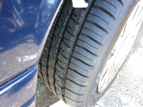 2001 Ford Crown Victoria - A close-up view of a blue car's tire and fender, showing the tread pattern and the vehicle's paint.