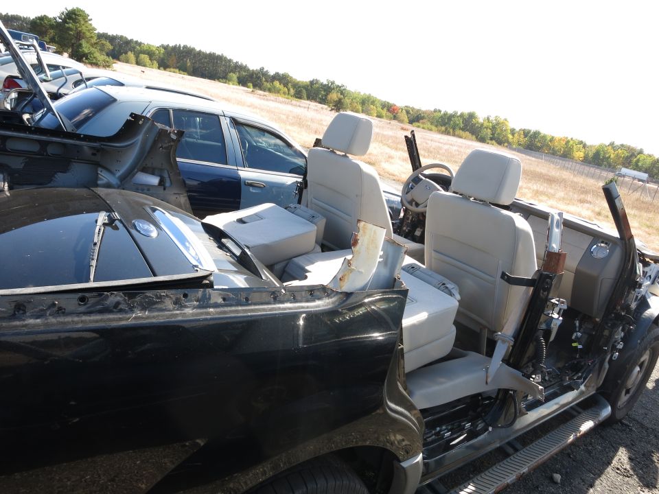 Interior of a wrecked black car with light-colored seats, showing exposed metal and a blue car in the background