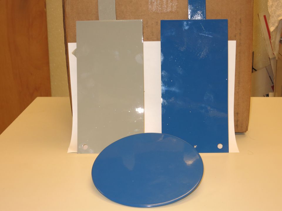 Two rectangular paint swatches, one gray and one blue, and a round blue swatch are on a table in front of a cardboard box