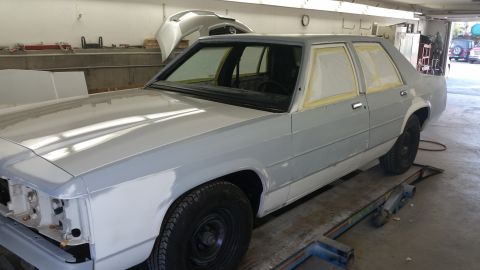 1991 Ford LTD Crown Victoria - A gray sedan is in a garage, with its windows taped off in preparation for painting.