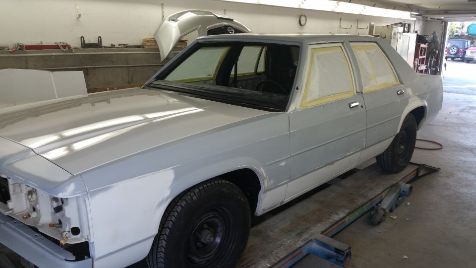 Gray sedan in garage, windows taped for paint. 3/4 front view