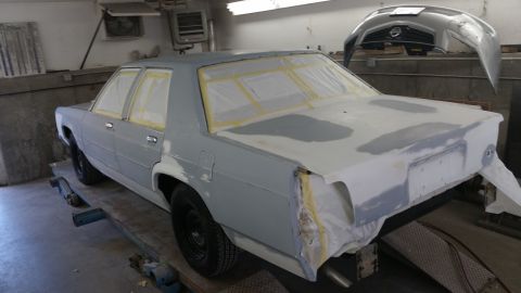 1991 Ford LTD Crown Victoria - A sedan is in a body shop, masked and prepped for paint, with a bumper hanging in the background.