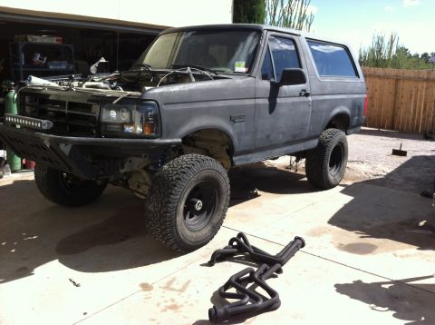 1995 Ford Bronco - A modified Ford Bronco sits outside a garage with its hood up and exhaust headers laid out nearby.