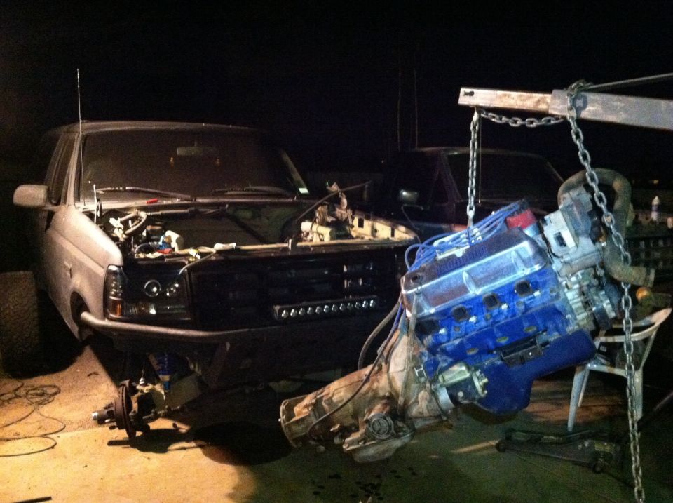 1995 Ford Bronco with hood open, engine being removed by a hoist. Front bumper is aftermarket