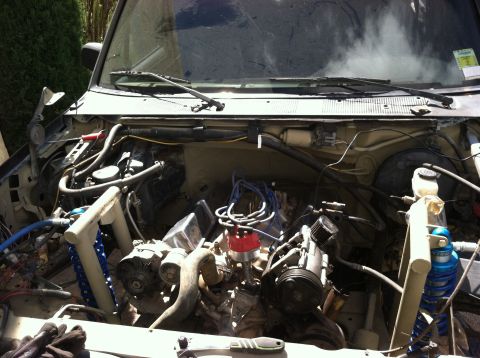 1995 Ford Bronco - The engine bay of a vehicle, showing the V8 engine, distributor, and suspension components, with some smoke or steam visible.