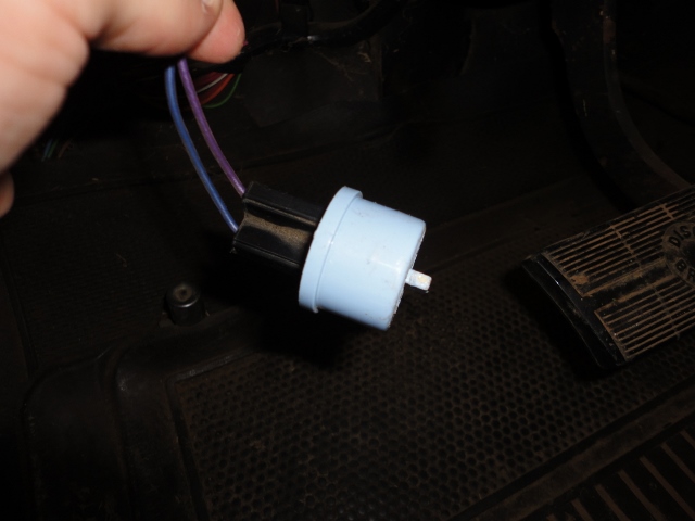 Light blue turn signal flasher relay and connector held above a truck's rubber floor mat