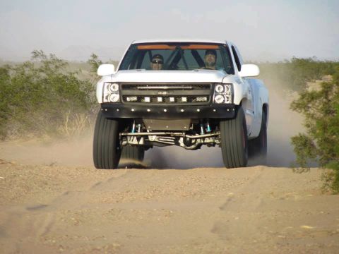 1968 Ford Mustang - A white off-road truck kicks up dust as it drives on a dirt path through a desert landscape.