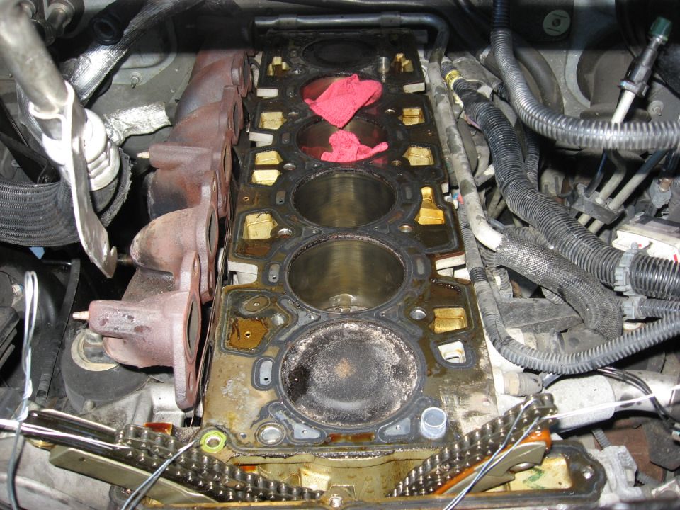 Engine block with exposed cylinders, exhaust manifolds, and timing chain. Red rags stuffed in cylinders