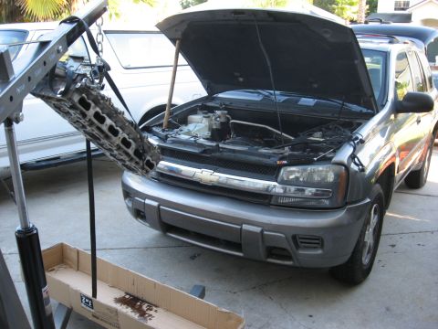 1994 Ford Bronco - Engine part suspended by a hoist over a gray Chevrolet Trailblazer with its hood open.