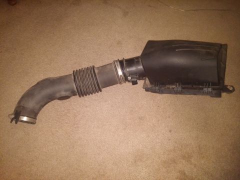 2000 Mercury Grand Marquis - This is an air intake system part, likely from a vehicle, lying on a carpeted surface.