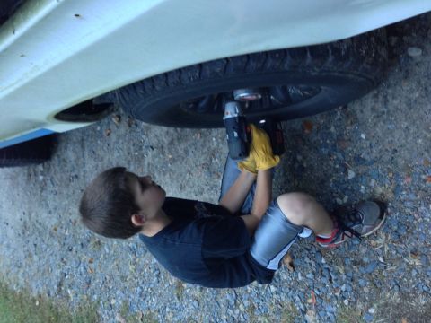 1979 Ford Bronco - Young mechanic works on a vehicle's wheel with a power drill.