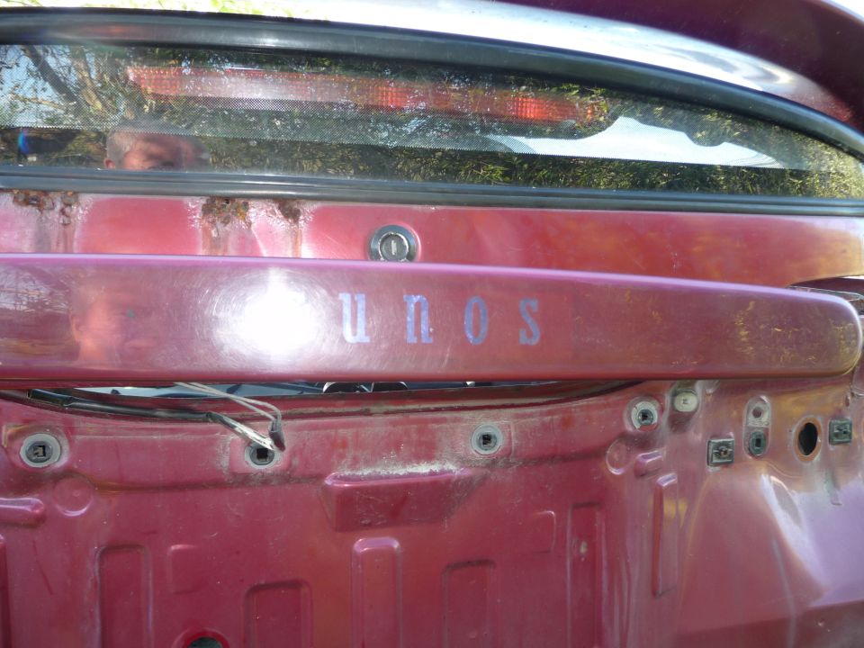 Rear panel of a red car with 'unos' lettering and exposed wires