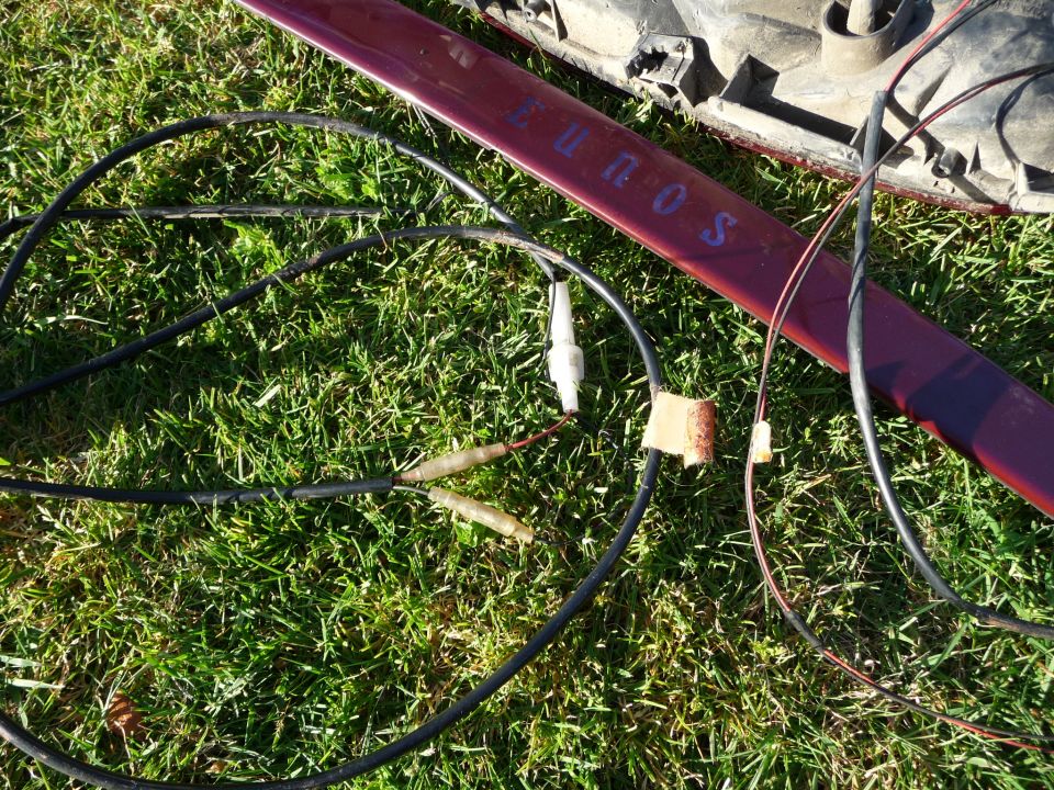 Maroon car part with 'Eunos' text and wiring harness laid on grass