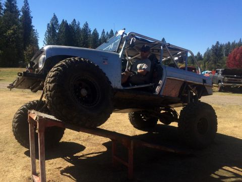1961 International Scout 800 - Modified off-road vehicle with extensive roll cage and large tires is positioned on a ramp, with another vehicle visible in the background.