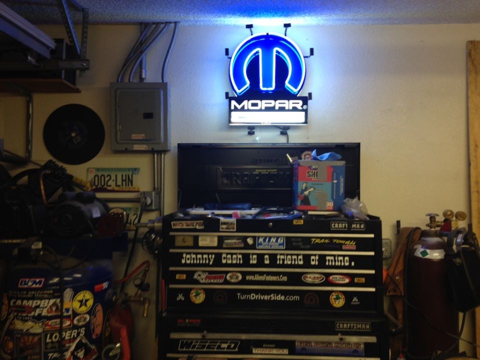 Mopar neon sign above a tool chest covered in stickers, including one that says 'Johnny Cash is a friend of mine.'